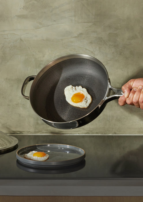 Serving egg with chrome Titanium Always Pan Pro onto black Salad Plate