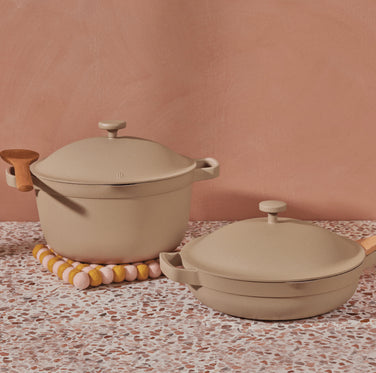 A beige Perfect Pot and Always Pan in front of a pink wall